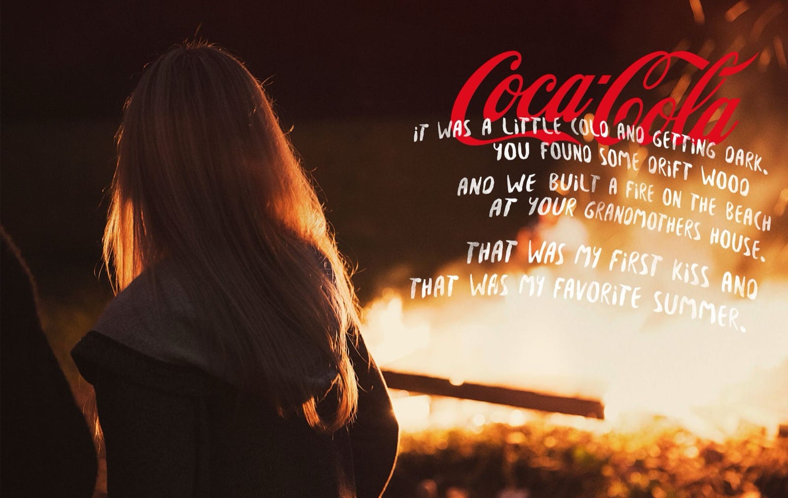 The Coca-Cola script over a beach bonfire at dusk, with handwritten copy about a first kiss and a favorite summer